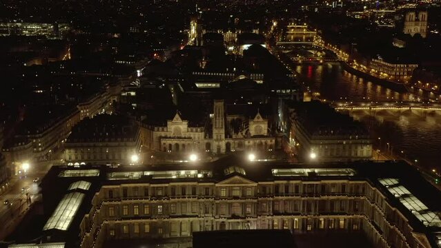Forwards fly above historic buildings of Louvre at Seine river waterfront. Illuminated streets in night city. Paris, France