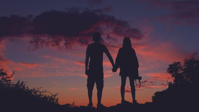 Silhouette of couple holding hands watching colorful sunset sky