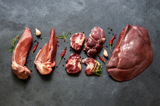 Raw beef giblets, kidney, liver and heart meat on stone rustic table with thyme and peppers
