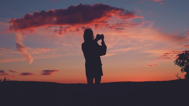 Silhouette of woman with camera taking photos at sunset