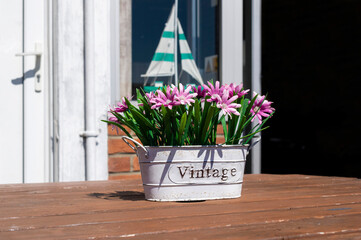 White vase with the word vintage and artificial pink flowers with green leaves on top of a wooden table. Decorative vase on a UK coffee shop table.