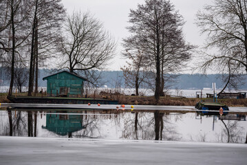 An old wooden green house on the shore of a freezing lake. Winter landscape. A melting ice sheet. A wooden house in the autumn scenery by the lake.