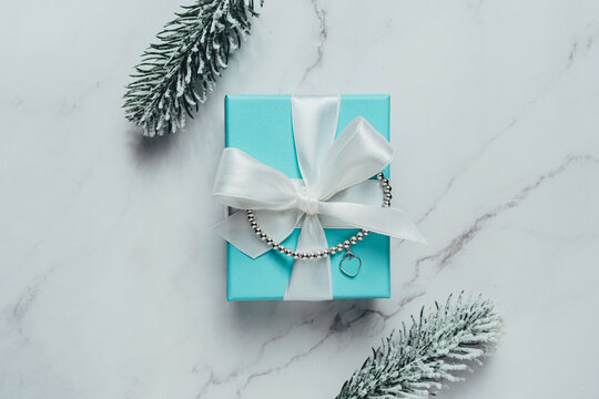 Barcelona, Spain - July 2022. Tiffany and Co branded gift box with heart bracelet from world-famous American fashion brand. Luxury, Christmas jewelry present on marble background with spruce twig