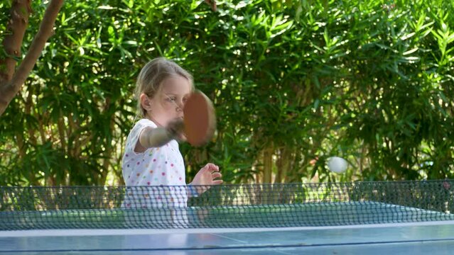 Girl play table tennis. Child player hit lightweight ping-pong ball back and forth across hard table divided by tennis net use small red rackets. Sport game is fast and demands quick reactions