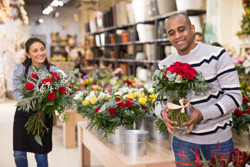 Fototapeta premium Experienced woman florist helping male client to choose flowers in flower shop