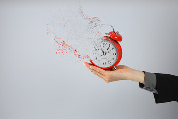 Time is running out. Woman holding vanishing red alarm clock against light grey background, closeup
