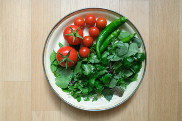 Organic some vegetables in a plate. Top view and copy space area with green vegetables and tomatoes.  Tomatoes, green pepper, mint, purslane, parsley and basil in a plate.