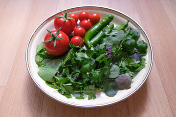 Organic some vegetables in a plate. Top view and copy space area with green vegetables and tomatoes.  Tomatoes, green pepper, mint, purslane, parsley and basil in a plate.