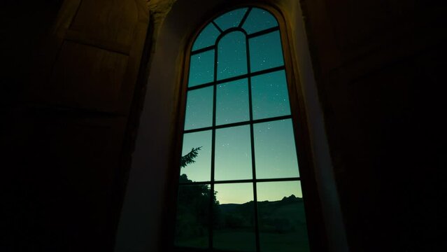 Time lapse of a starry night sky through an arched chapel window