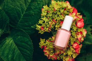 Organic natural nail polish bottle on flowers background, top view.