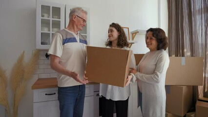 Senior parents help daughter with relocation to new apartment. Elderly couple stands in kitchen waving goodbye to woman walking away with paper bag