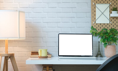Comfortable workplace with laptop computer, coffee cup, books, houseplant and lamp. Empty display for your advertise text.