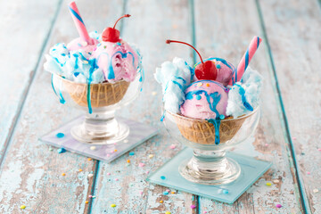 Two cotton candy sundaes in waffle bowls topped with sprinkles and syrup.
