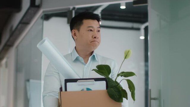 Dismissal and unemployment. Upset fired mature asian man standing at office, carrying box with personal belongings