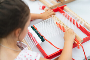 Girl weaving small rug with pattern at masterclass on weaving. Girl is studying how to weave on manual table loom. Process of creation. Handmade concept