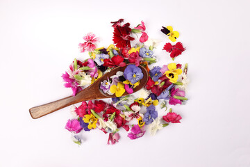 Beautiful colourful yellow violet wite red edible flowers wooden spoon on white background copy text space