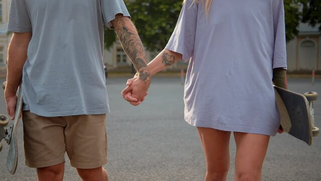 Active couple walking tattoo hand in hand. romantic moment between two lovers walk in street w skateboard. Concept love two people, relationship lifestyle hands of couple love walk through spring city