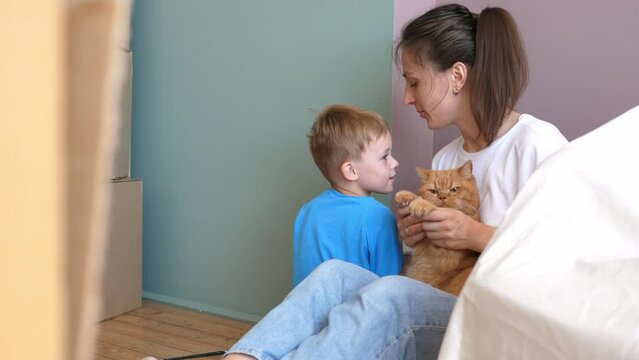 Young mother, a funny child and a ginger cat have fun during the renovation. Renovation of the rooms of the house, cardboard boxes, a new house and moving.