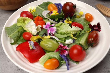 Beautiful colourful yellow violet wite red edible flowers on greed garden salad tomato marble table top bowl wooden spoon on white background copy text space