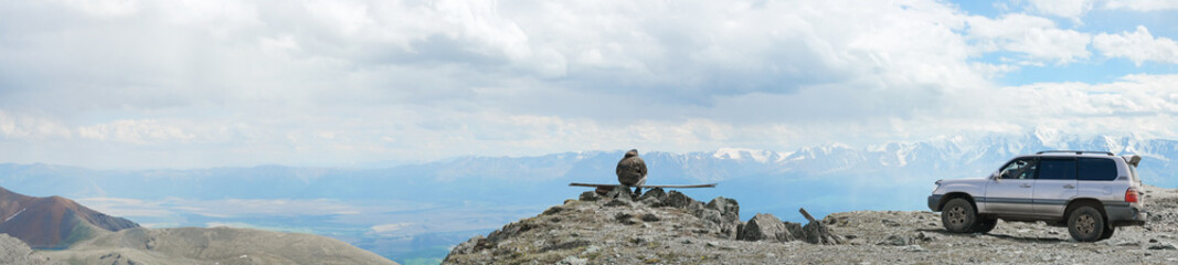 Dramatic panoramic landscape of rocky mountains among the clouds. Faceless tourist and his car high...