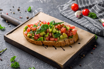 bruschetta with tomatoes and avocado on the board on grey table