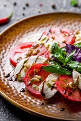 Caprese salad with mozzarella and tomato with basil and cream balsamic on brown plate vertical