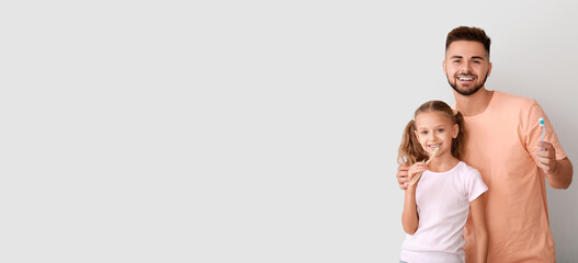 Portrait of happy man and his little daughter brushing teeth on light background with space for text