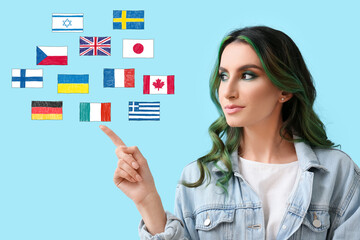 Pretty young woman and different flags on light blue background. Studying of foreign languages
