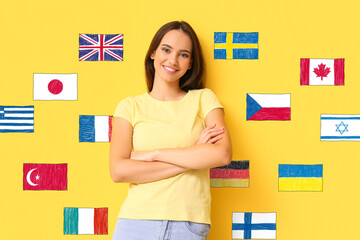 Beautiful young woman and different flags on yellow background. Studying of foreign languages