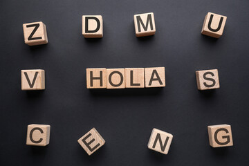 Word HOLA (HELLO) made of wooden cubes on dark background, top view