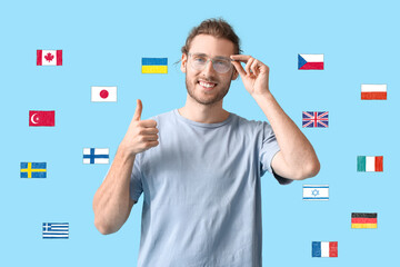 Young man showing thumb-up and many different flags on light blue background. Studying of foreign...