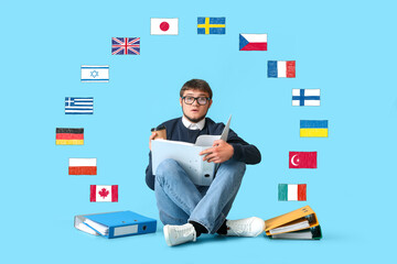 Young male student with many folders and different flags on light blue background. Studying of...
