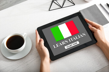 Woman holding tablet computer with text LEARN ITALIAN on screen at workplace - obrazy, fototapety, plakaty