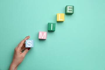 Female hand and cubes with word SMILE on color background