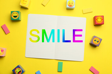 Fototapeta na wymiar Open notebook with word SMILE and cubes with emoticons on yellow background