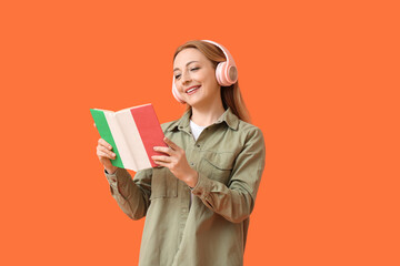 Mature woman with headphones reading book on orange background. Concept of studying Italian language