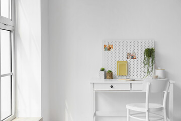 Modern workplace with pegboard, notebooks and houseplants near light wall