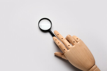 Wooden hand and magnifying glass on light background