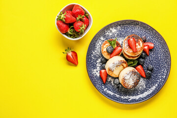 Plate with cottage cheese pancakes and bowl with fresh strawberry on yellow background