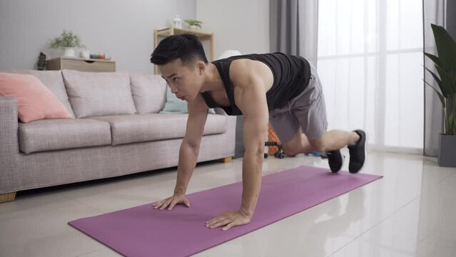 asian powerful male is doing ab exercise mountain climbers with full concentration on the yoga mat during daytime in the living room at home.