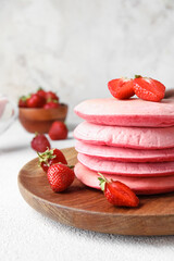 Wooden plate of tasty pink pancakes with strawberry on light background, closeup