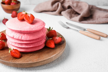 Wooden plate of tasty pink pancakes with strawberry on light background, closeup