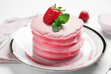 Plate of tasty pink pancakes with strawberry on table, closeup