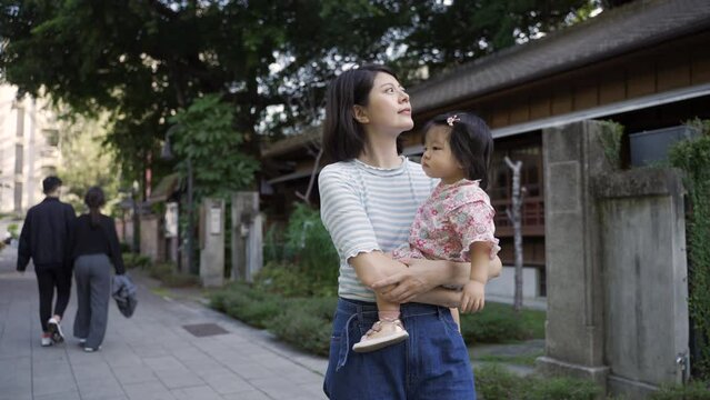 asian mother with her curious toddler daughter who's wearing japanese kimono in her arms are enjoying walking around neighborhood at leisure on a sunny day.