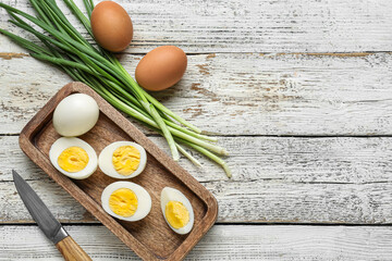 Board with boiled chicken eggs and green onion on light wooden background
