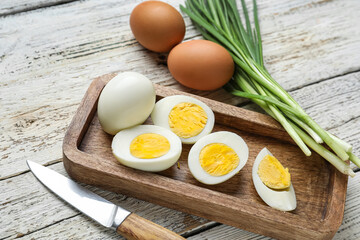 Board with boiled chicken eggs and green onion on light wooden background