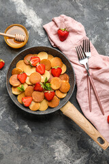 Composition with frying pan of mini pancakes, strawberry and honey on grunge background