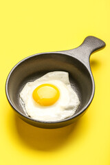 Frying pan with tasty egg on yellow background