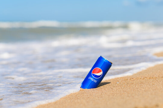 Anapa, Russia - July 2022: A can of Pepsi Cola drink on the sandy seashore against the backdrop of waves. Selective focus on a can of drink.