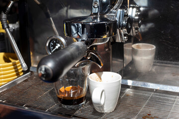 Espresso pouring into glass and cup in coffee cafe from portafilter of coffee machine.